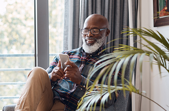 Shot of a mature man using a cellphone while relaxing on a sofa at home